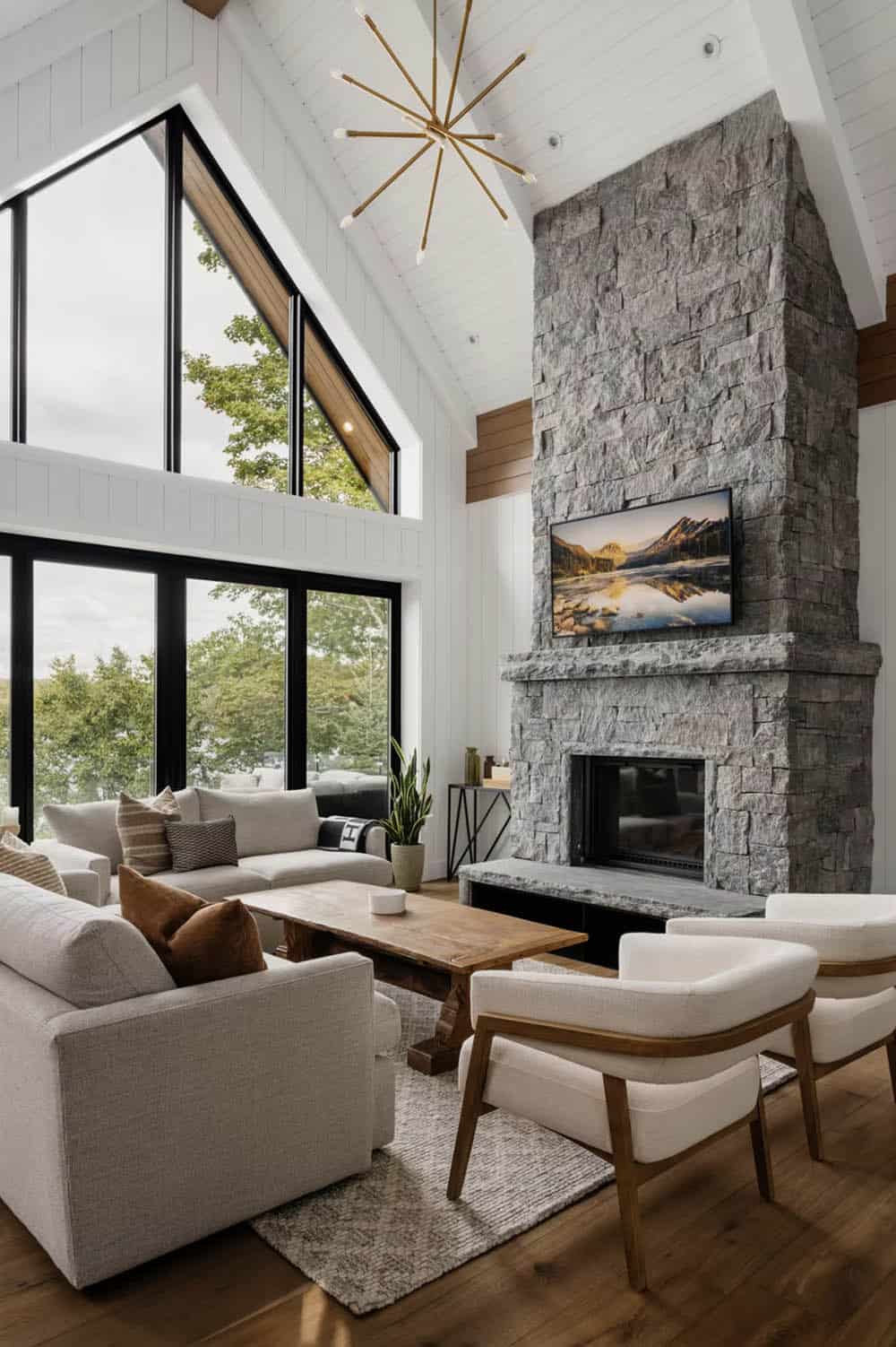 Vaulted great room with floor-to-ceiling stone fireplace, Sputnik chandelier, and triangular lakeside windows