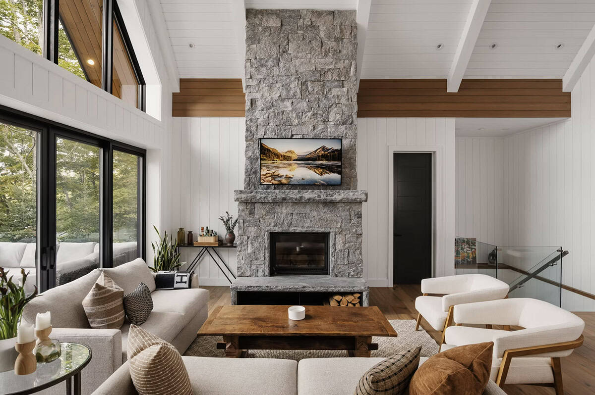 Living room with full-height stone fireplace, exposed wood beams, shiplap walls, and glass stair railing