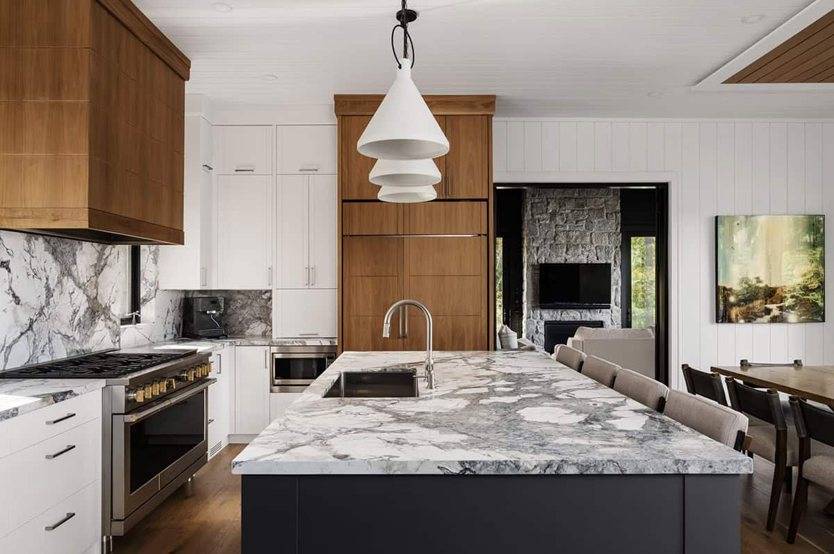 Kitchen with dramatic marble backsplash, wood range hood, dark island, and white cone pendant lights