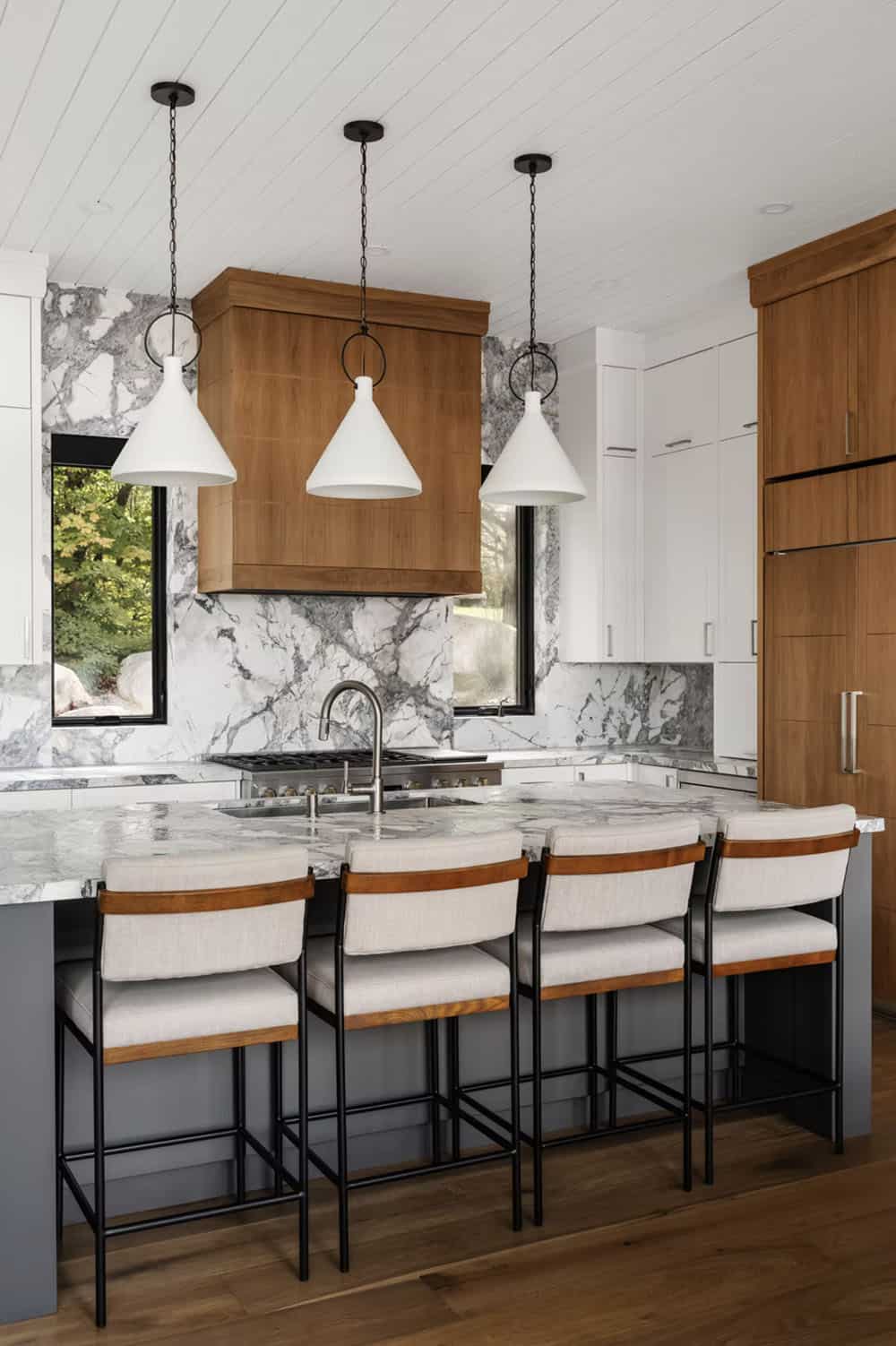 Kitchen island with bold marble countertop, four upholstered bar stools, and white cone pendants