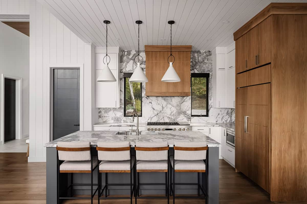 Kitchen with marble backsplash wall, warm wood cabinetry, dark island, and white pendant lights