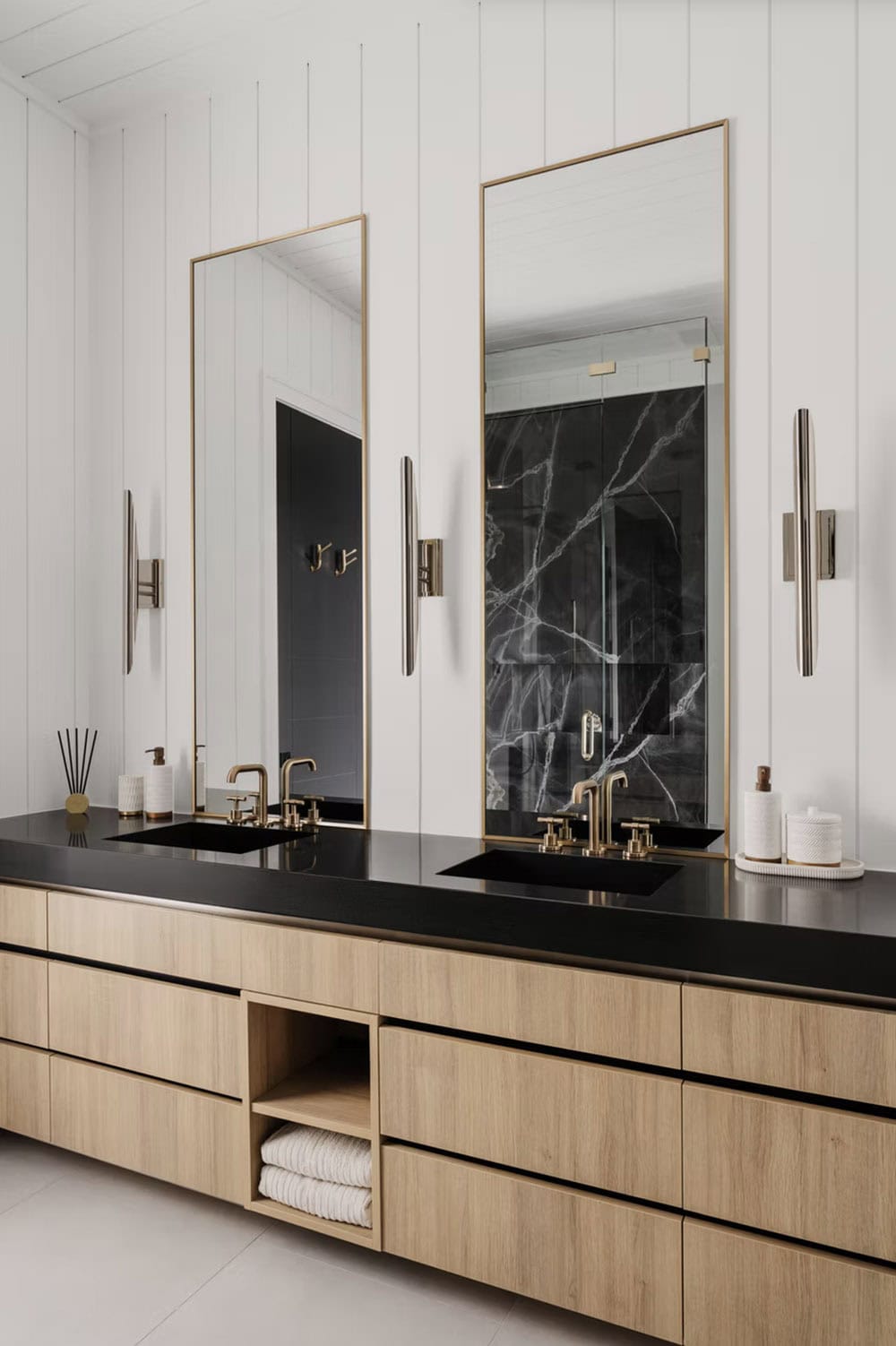 Primary bathroom double vanity with black countertop, brass fixtures, gold-framed mirrors, and shiplap walls