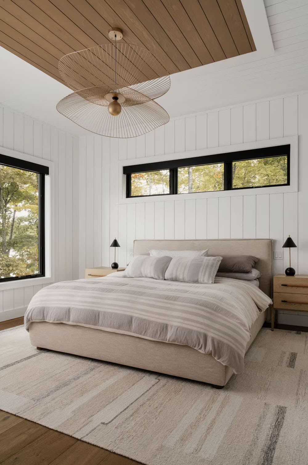 Primary bedroom with gold wire pendant light, wood ceiling inset, shiplap walls, and treetop views