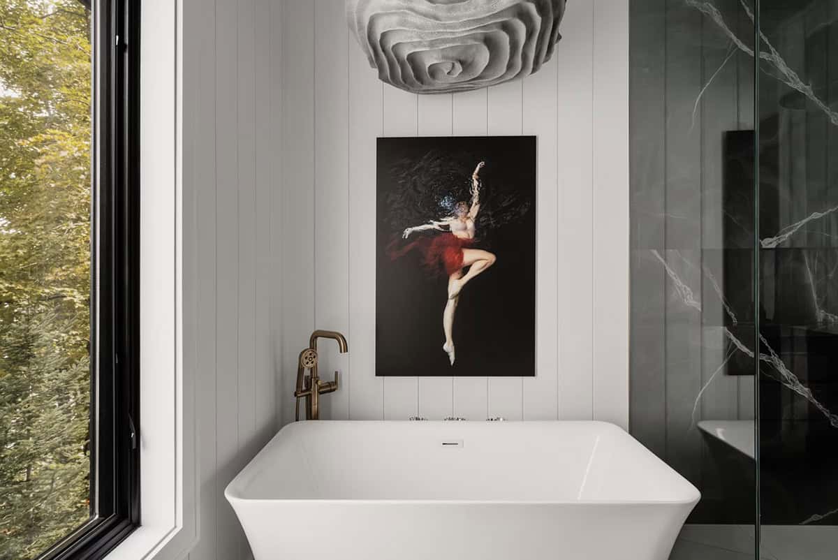 Freestanding soaker tub with brass fixtures beside forest window and dark marble shower enclosure