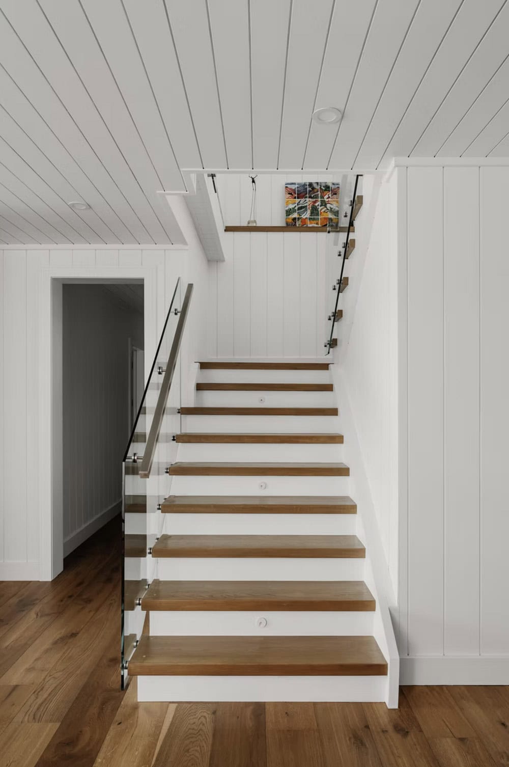 Open-riser wood staircase with glass panel railing and shiplap walls