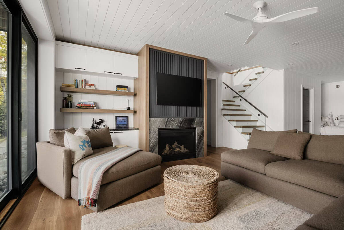 Lower-level family room with wood-framed fireplace, built-in shelves, wicker ottoman, and glass stair railing