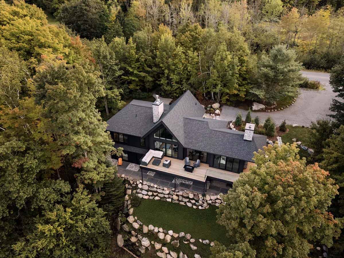 Aerial view of black cottage surrounded by fall foliage with wood deck and stone retaining wall