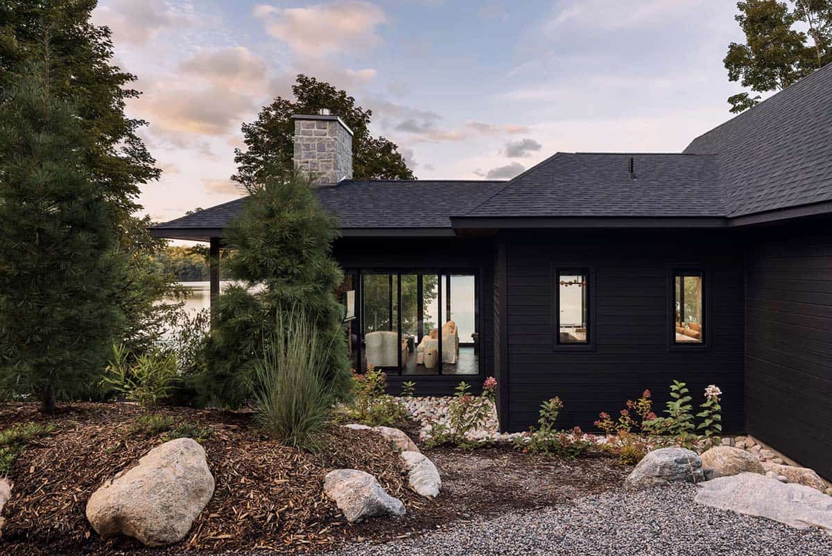 Black cottage exterior at dusk with lakeside garden, boulder landscaping, and sunroom addition