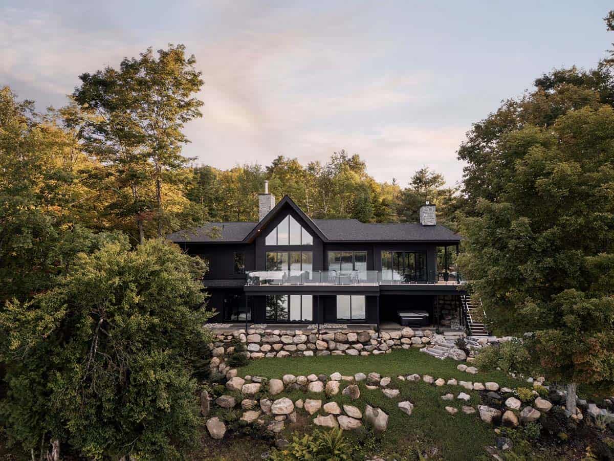Black cottage rear elevation framed by autumn trees with large gabled window and upper deck