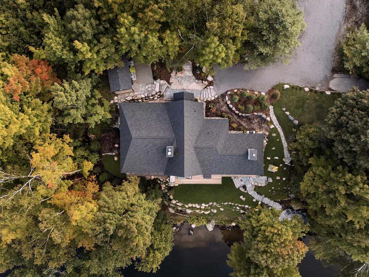 Aerial overhead view of cottage roof and property showing lake, driveway, and natural stone landscaping