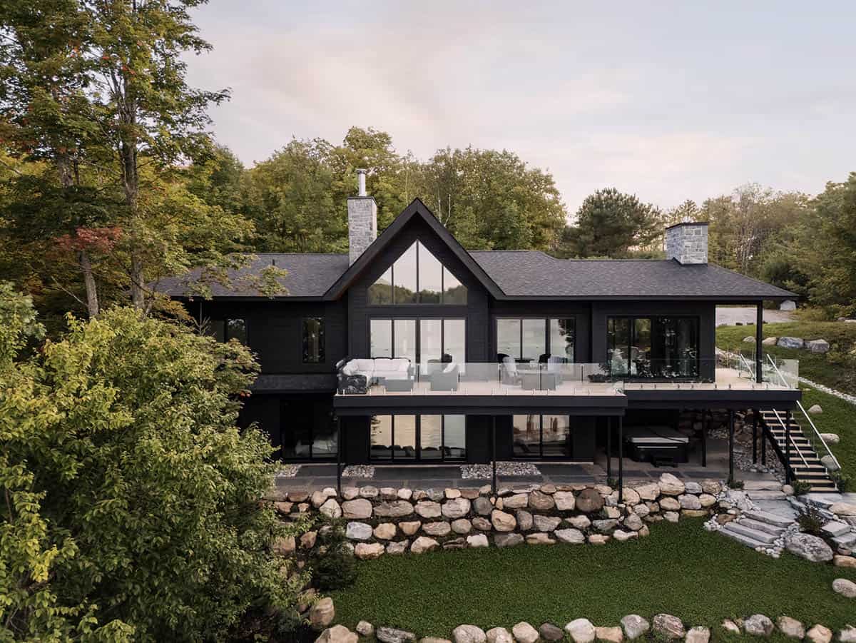 Black cottage rear exterior with upper deck seating, gabled window wall, and tiered stone lawn