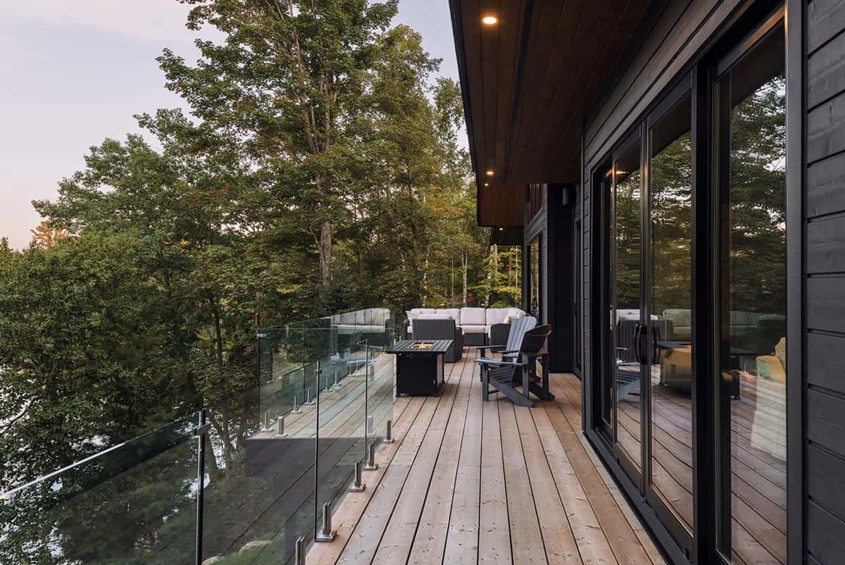 Elevated wood deck with glass railing, fire table, and Adirondack chairs overlooking forest treetops