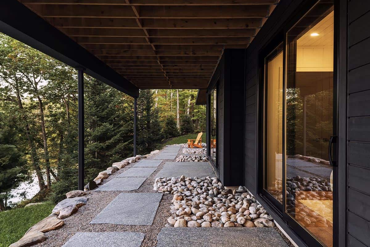 Covered lower walkway with stone pavers, river rock edging, and Adirondack chair overlooking lake