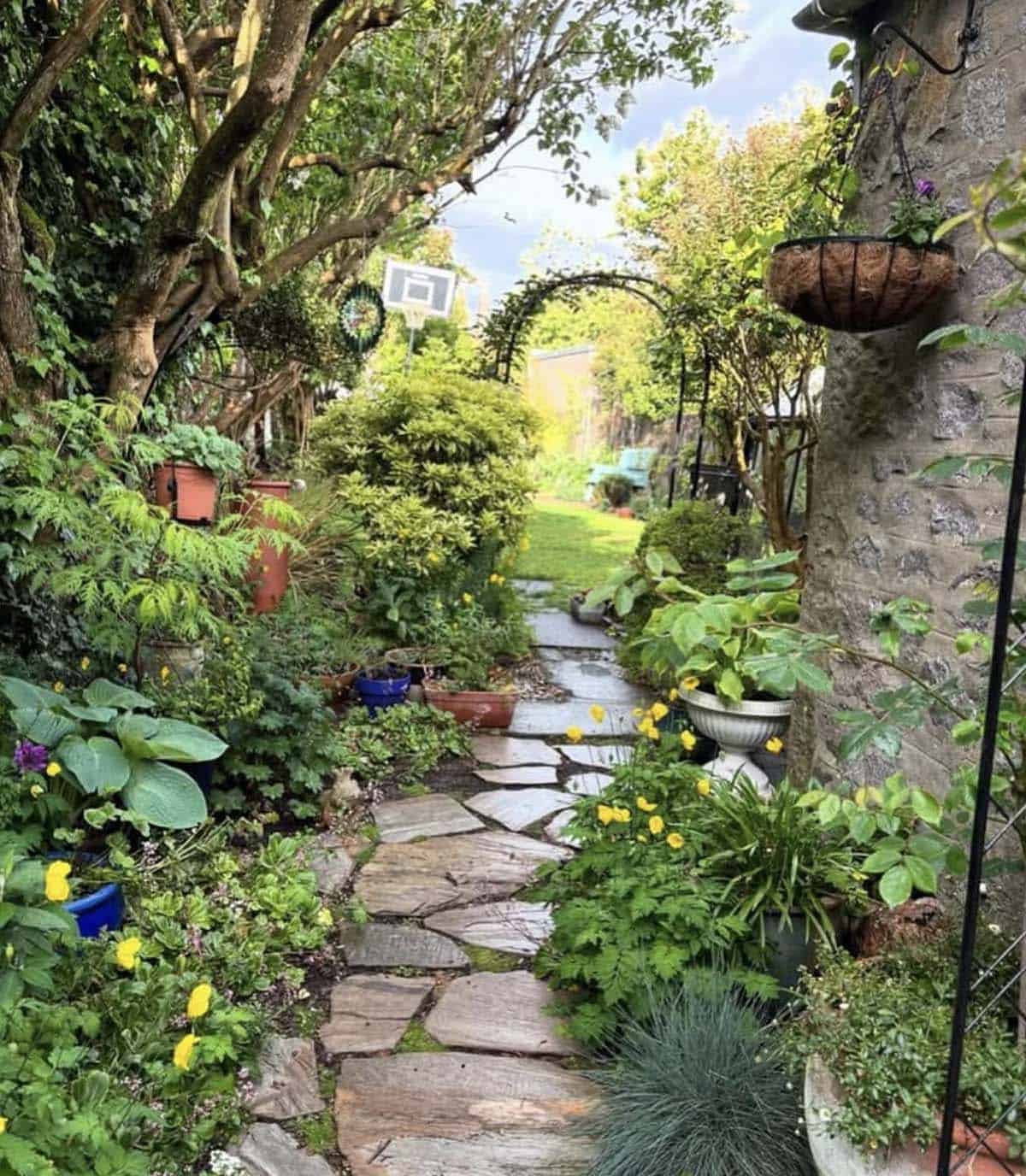 Narrow side yard with irregular flagstone path, lush plantings, and metal garden arch