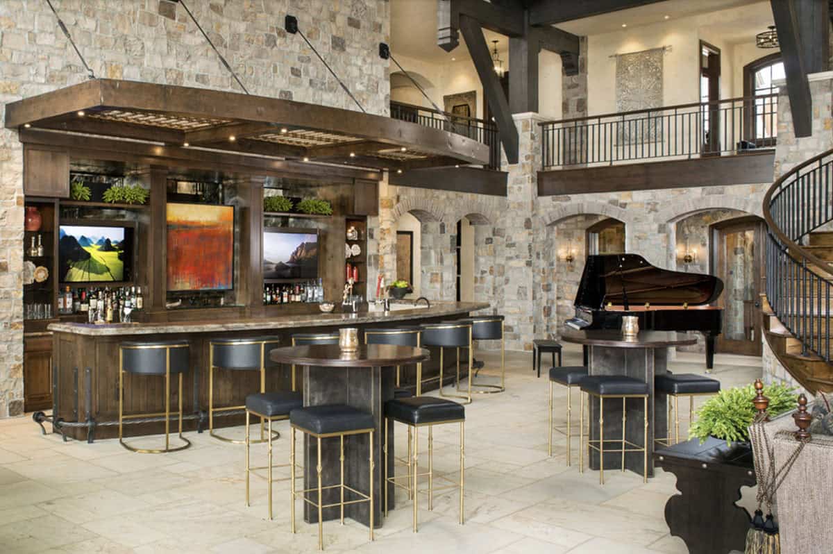Full-service bar with grand piano, stone arches, and curved staircase