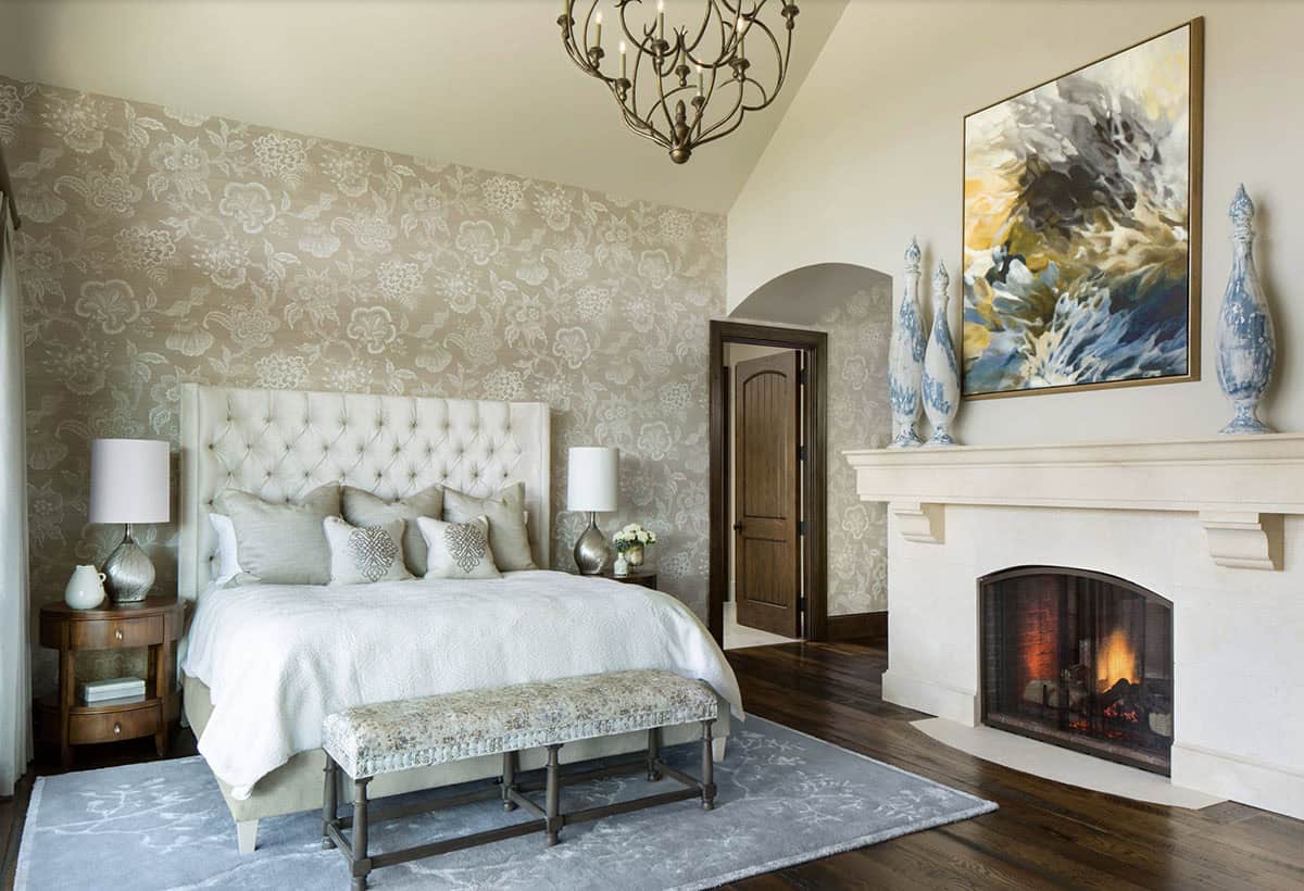 Primary bedroom with tufted headboard, floral wallpaper, and cast stone fireplace
