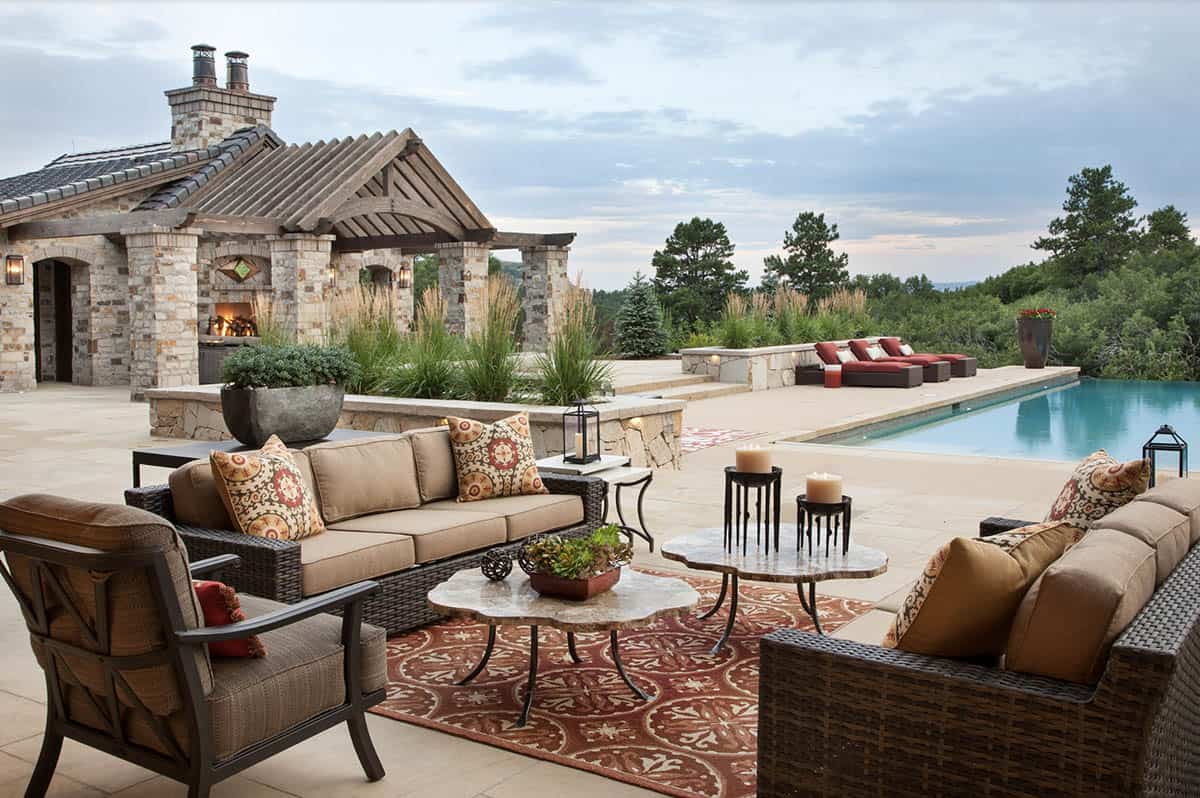 Pool deck lounge area with wicker seating, stone pool house, and infinity pool at dusk
