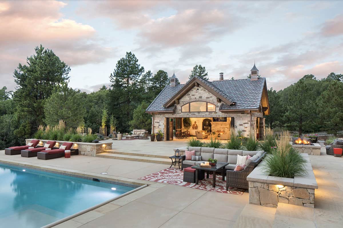 Stone pool house exterior at dusk with open garage doors, pool, and fire pit