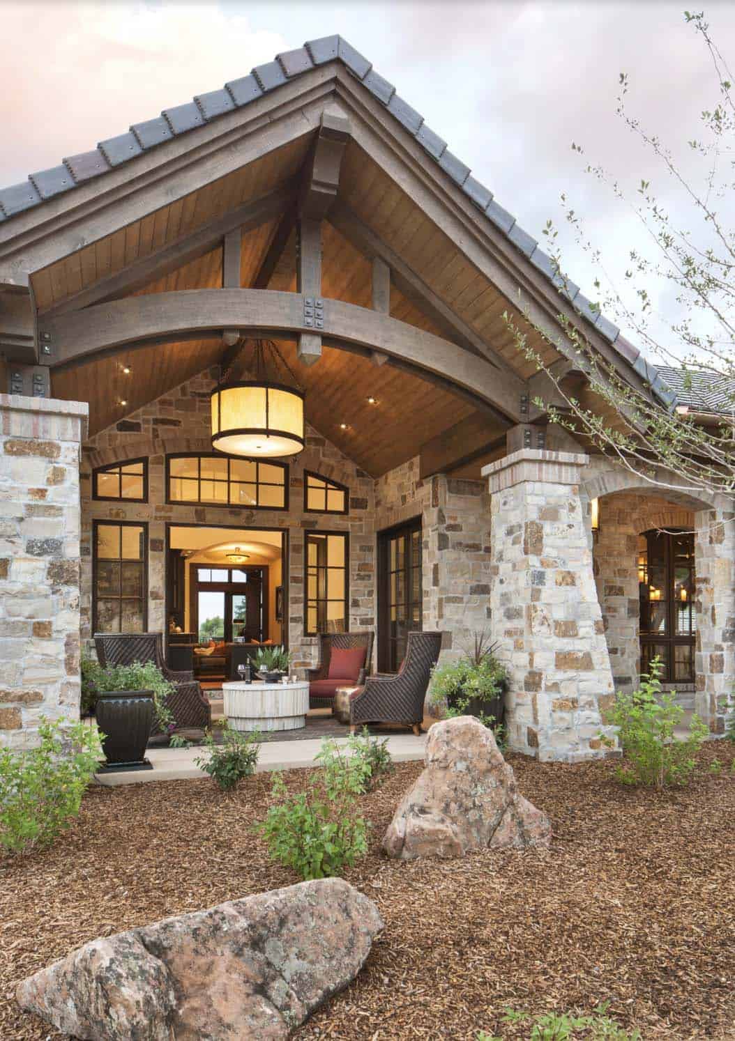 Natural stone exterior entry with wood truss porte-cochere at dusk