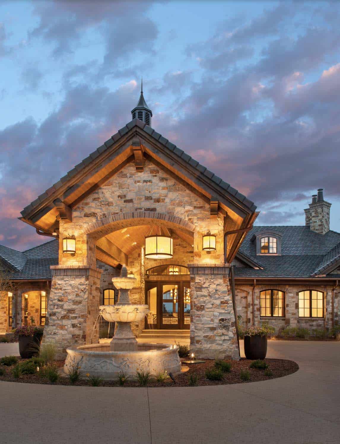 Front entrance at dusk with stone fountain, arched entry, and cupola roofline