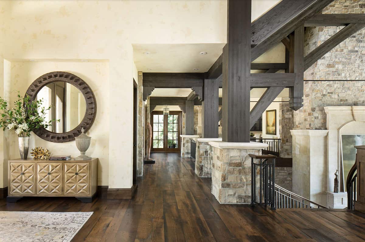 Entry hallway with wood beam columns, stone accents, dark hardwood floors, and round mirror