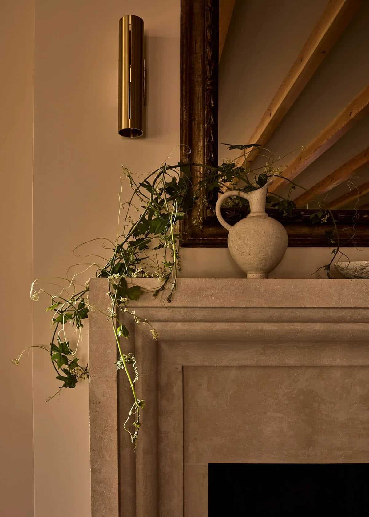 Stone fireplace mantel with trailing vines and antique brass sconce