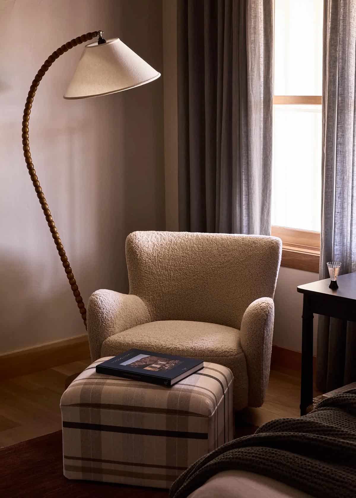 Reading nook with boucle armchair, plaid ottoman, and beaded arc floor lamp