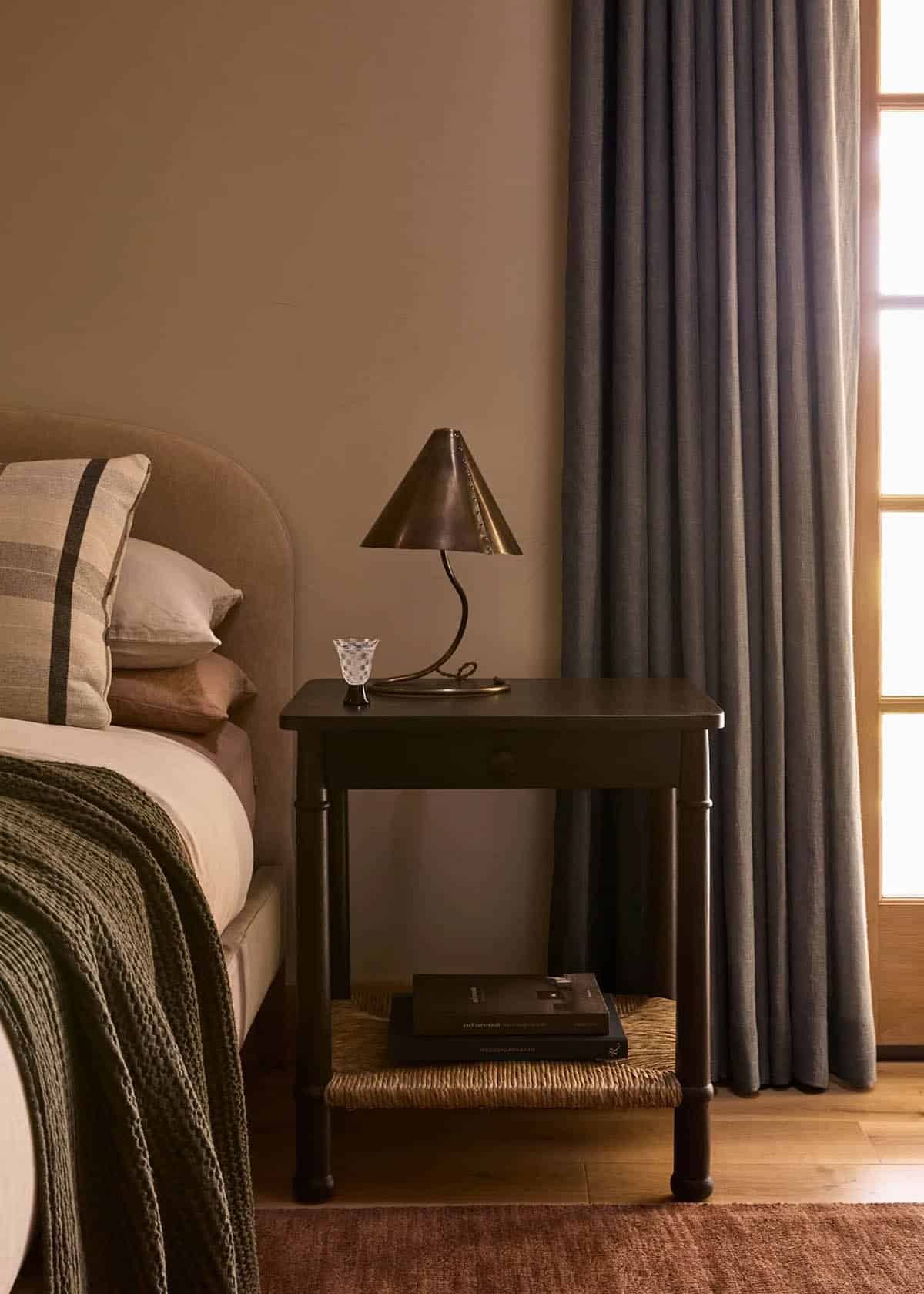 Primary bedroom nightstand with brass table lamp and linen drapes