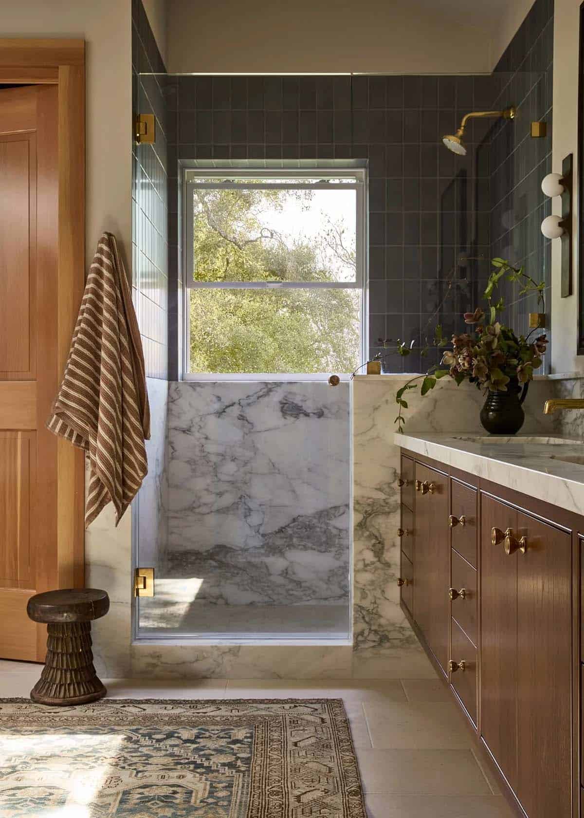Primary bathroom with dark tile shower, marble vanity, and vintage rug