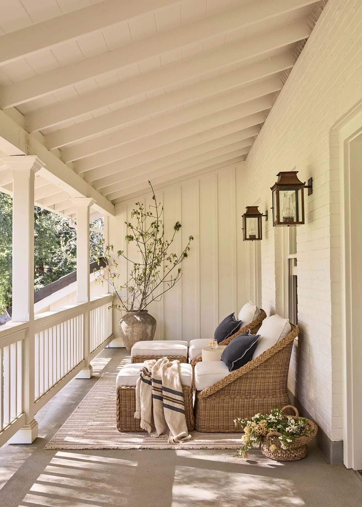 Covered porch with wicker seating, copper lanterns, and orchard views
