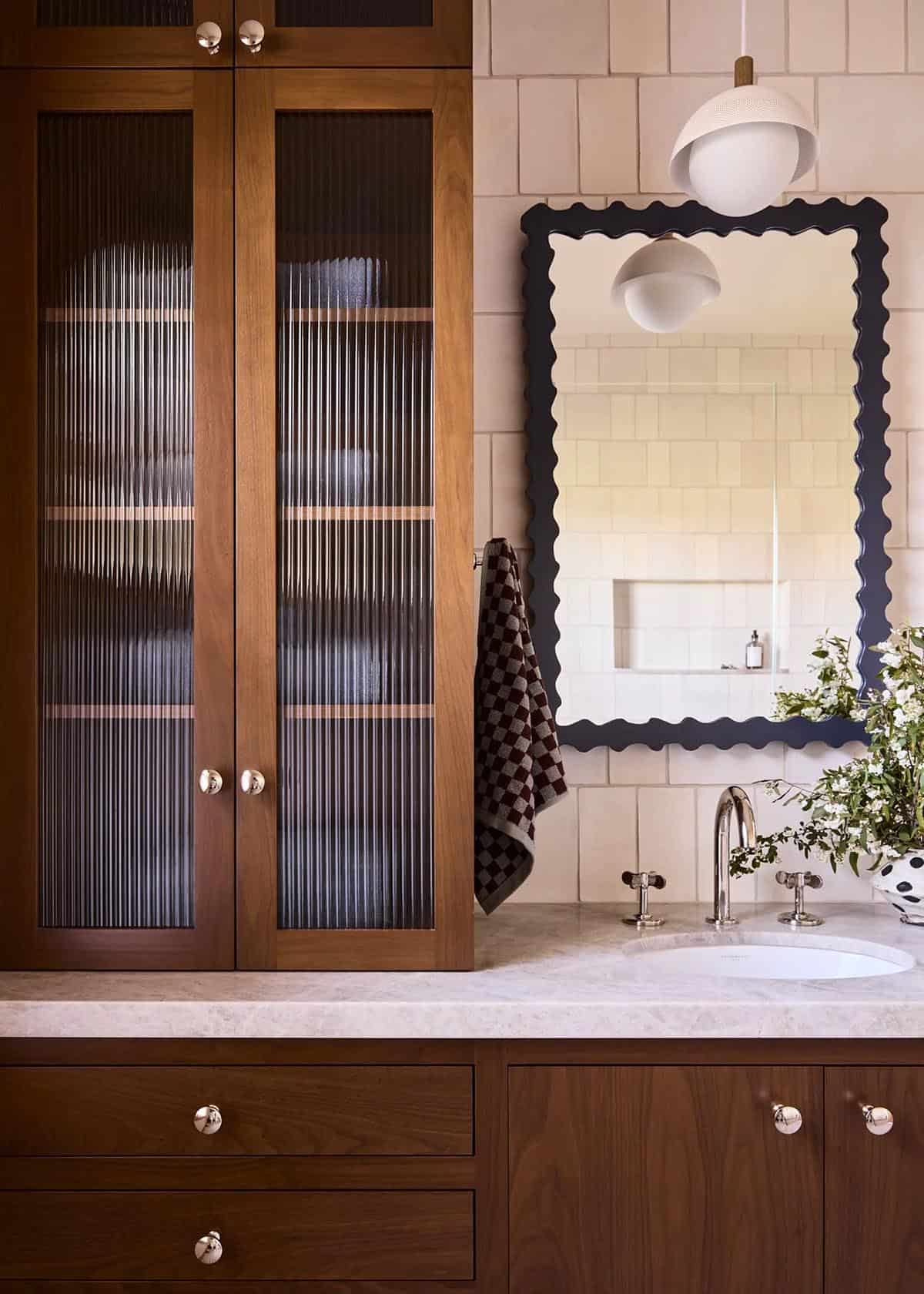 Kids bathroom with walnut cabinetry, scalloped mirror, and cream tile
