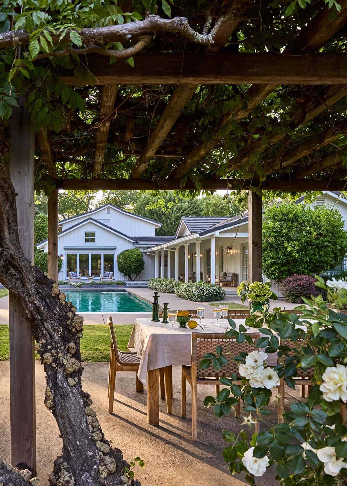 Outdoor dining under vine-covered pergola overlooking pool and farmhouse