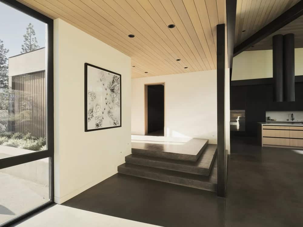 Open interior hallway with concrete steps, wood ceiling, framed artwork, and view toward dark kitchen
