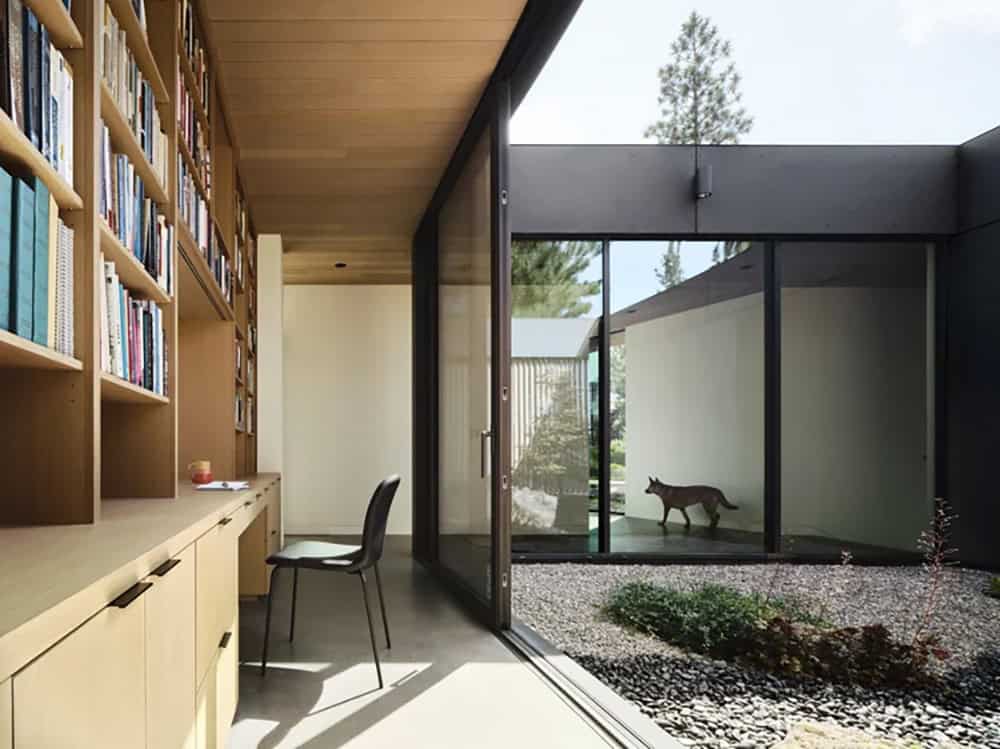Home office with floor-to-ceiling built-in bookshelves overlooking a gravel courtyard