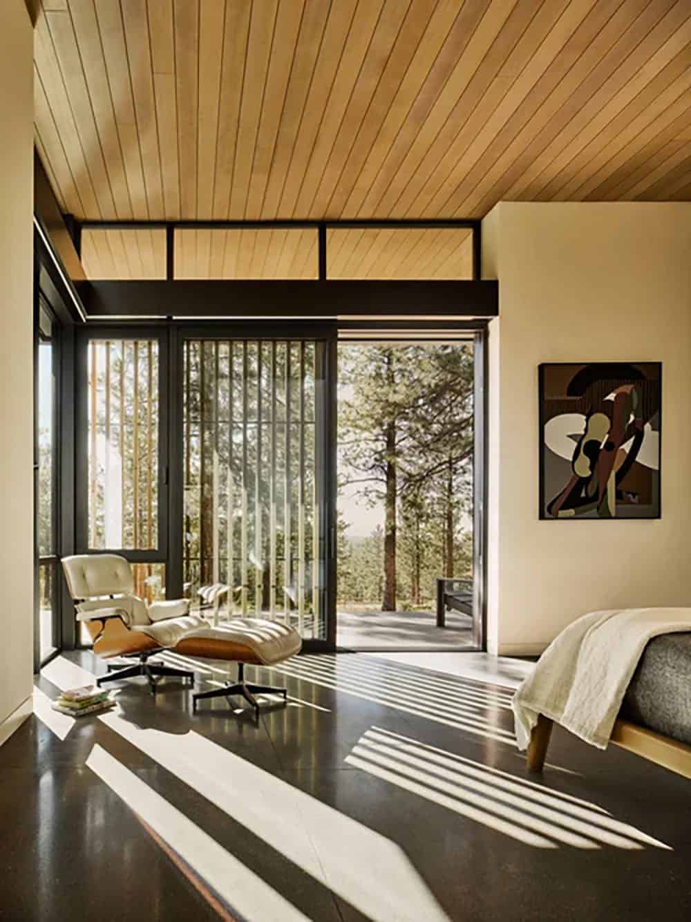 Bedroom with Eames lounge chair, dark hardwood floor, and sliding glass doors opening to forest views