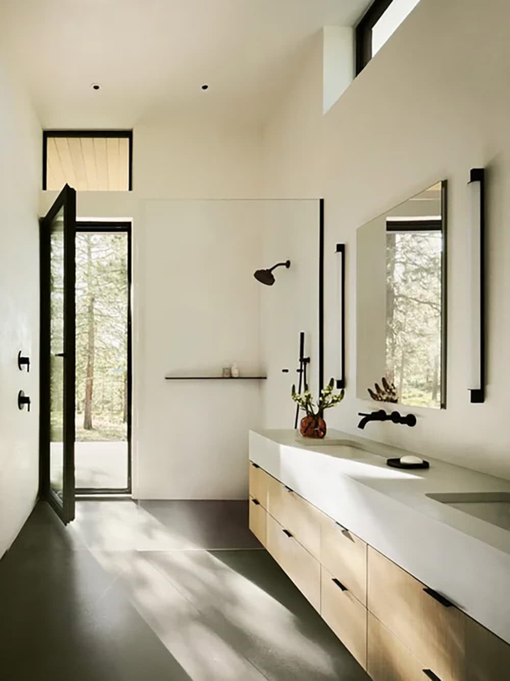 Minimalist bathroom with floating wood vanity, black fixtures, and narrow windows framing pine trees