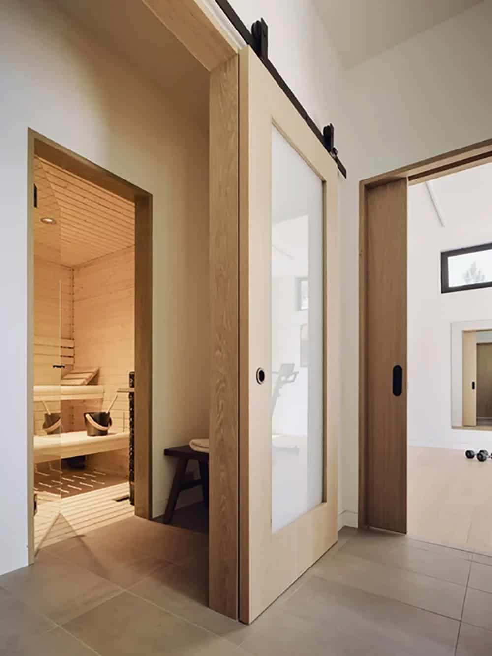 Hallway with light wood barn door opening to a cedar-lined sauna with tiered benches