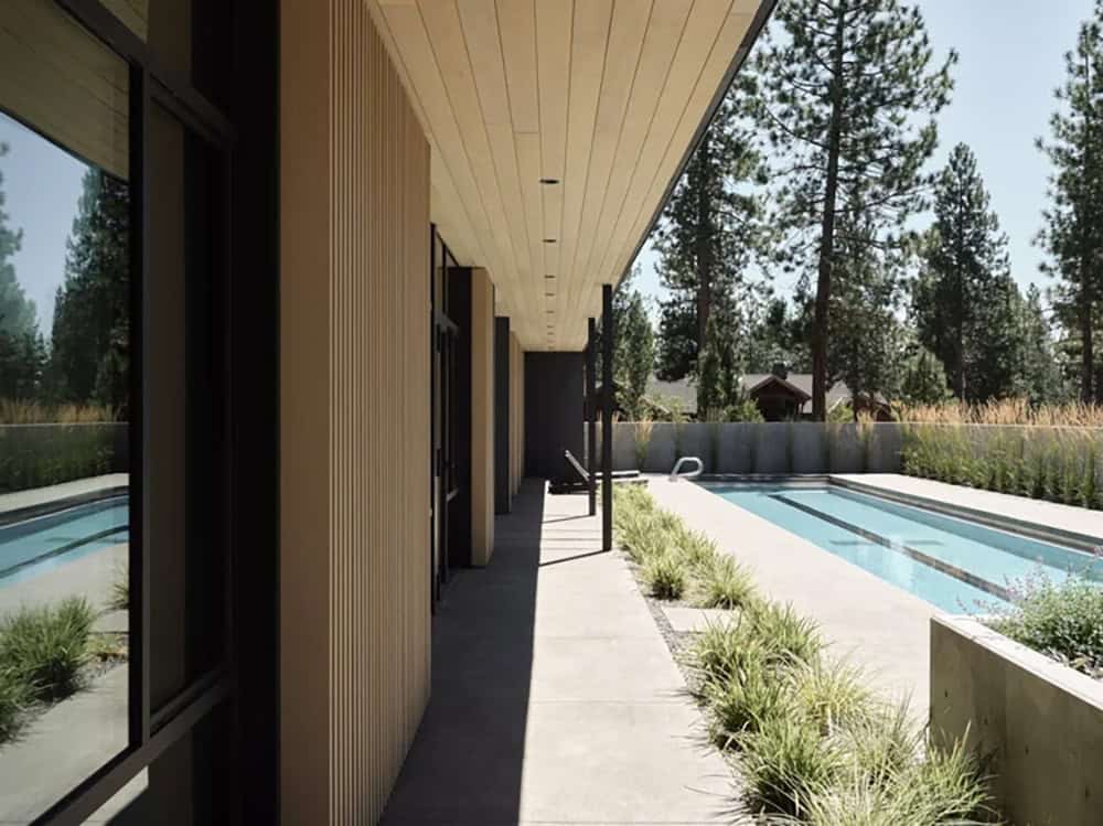 Covered poolside walkway with vertical wood siding, black-framed windows, and lap pool alongside
