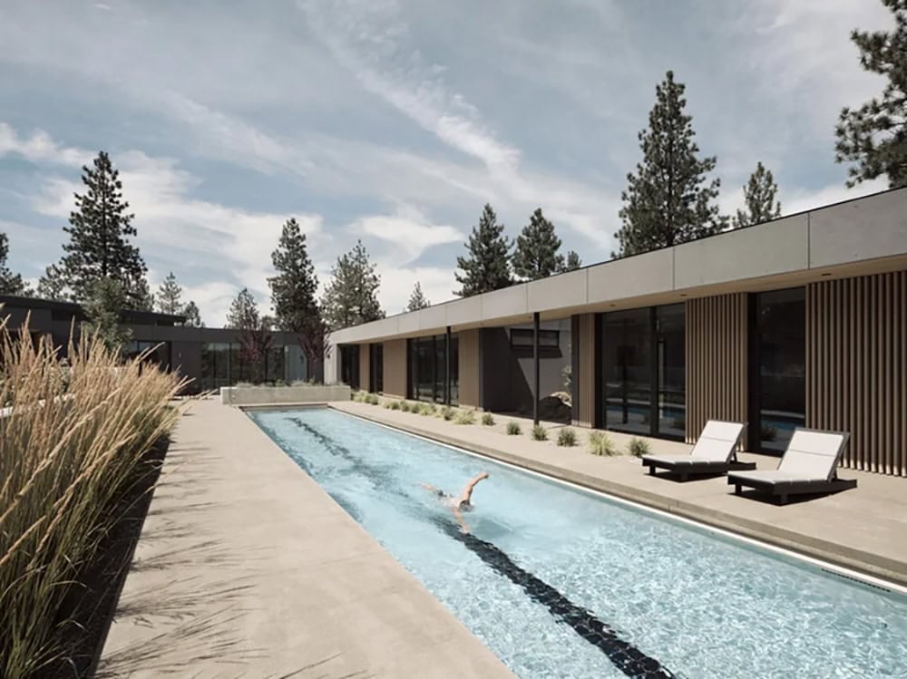 Swimmer doing laps in a long narrow pool beside a horizontal modern home with vertical wood cladding