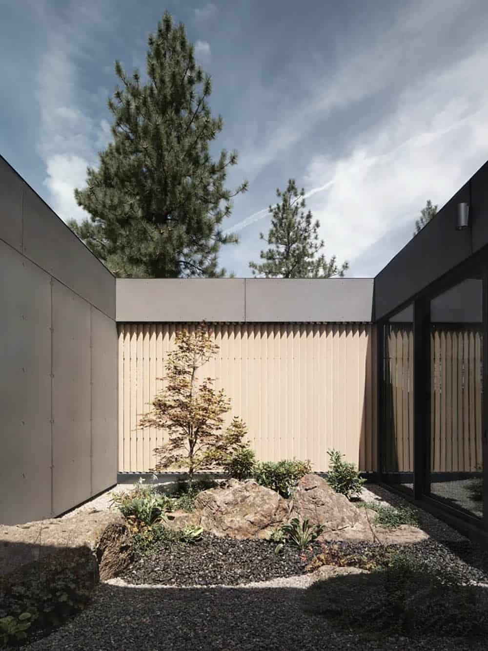 Enclosed courtyard with Japanese maple, volcanic rocks, and gravel against vertical wood slat cladding