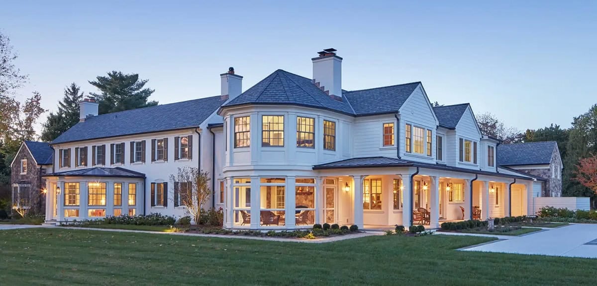 Historic waterfront house renovation with faceted sunroom, screened porch and bay windows at dusk on the Chesapeake Bay in Maryland