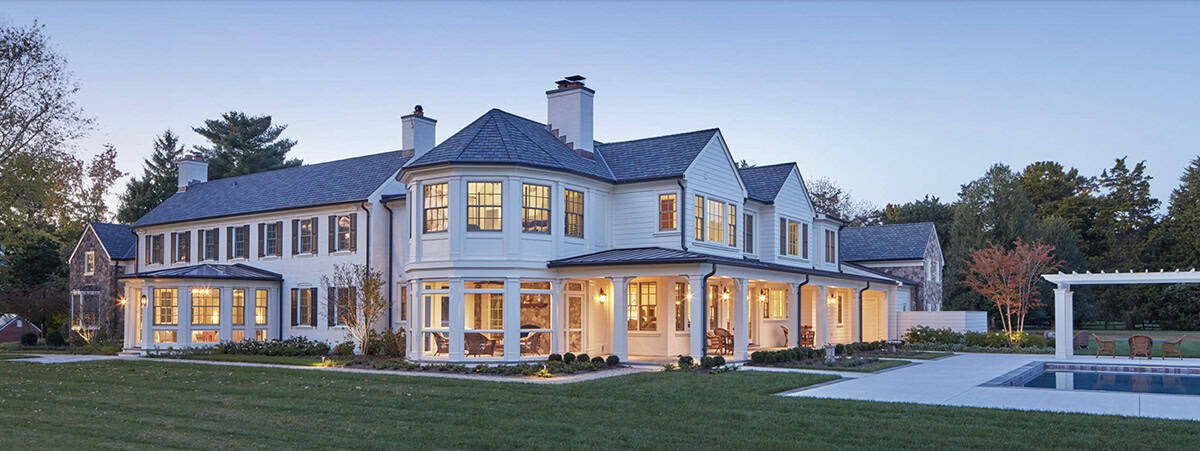 Historic waterfront house renovation rear exterior with faceted sunroom, screened porch and pool at dusk on the Chesapeake Bay in Maryland