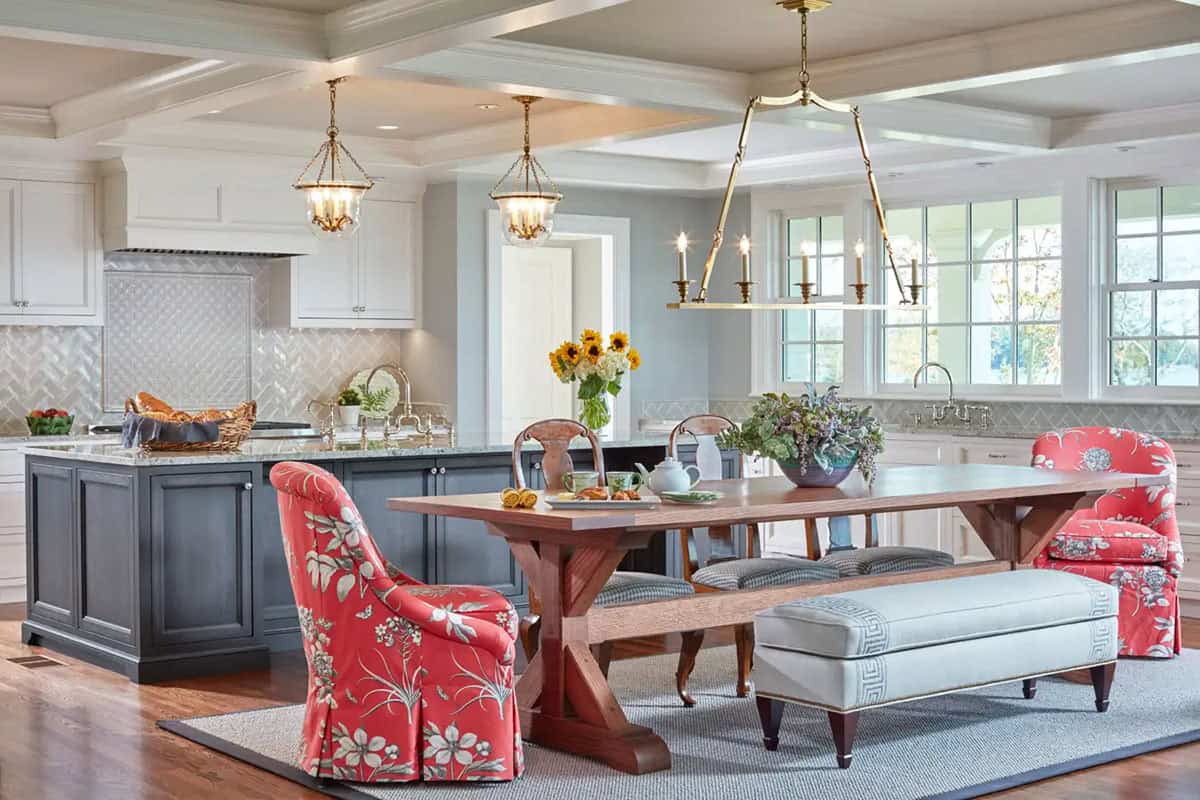 Historic waterfront house open kitchen with coffered ceiling, gray island, brass chandeliers and colorful upholstered dining chairs in Maryland