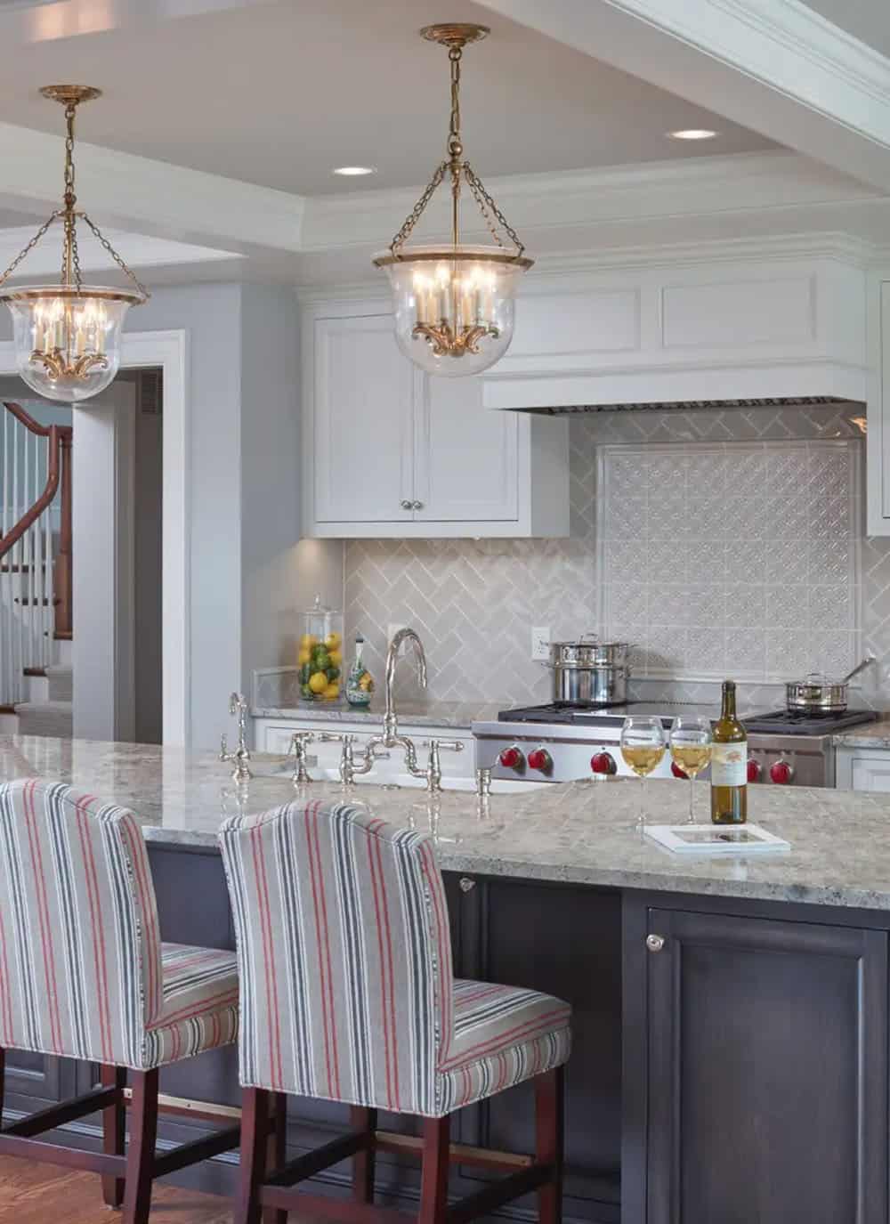 Historic waterfront house kitchen with gray island, herringbone tile backsplash, striped bar stools and brass pendant lights in Maryland