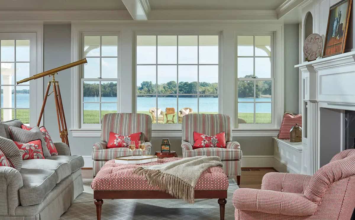 Historic waterfront house sunroom with Chesapeake Bay views, striped armchairs, red upholstered ottoman and brass telescope in Maryland