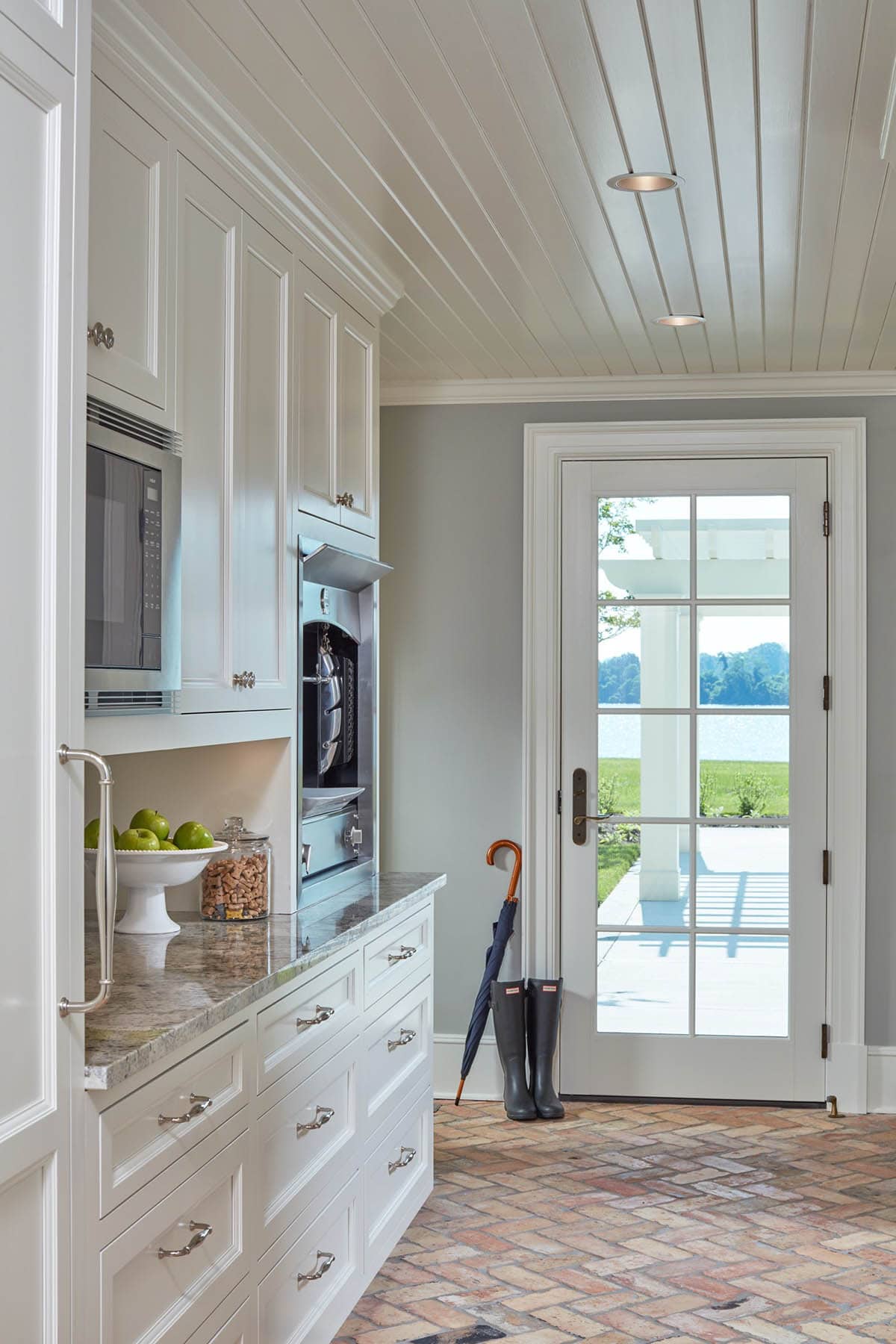 Historic waterfront house butler's pantry with white cabinetry, granite countertop, herringbone brick floor and glass door to pool terrace in Maryland
