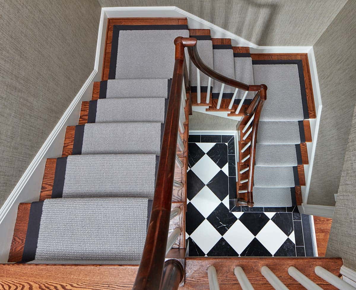 Historic waterfront house staircase with gray carpet runner, mahogany banister and black and white diamond marble floor below in Maryland