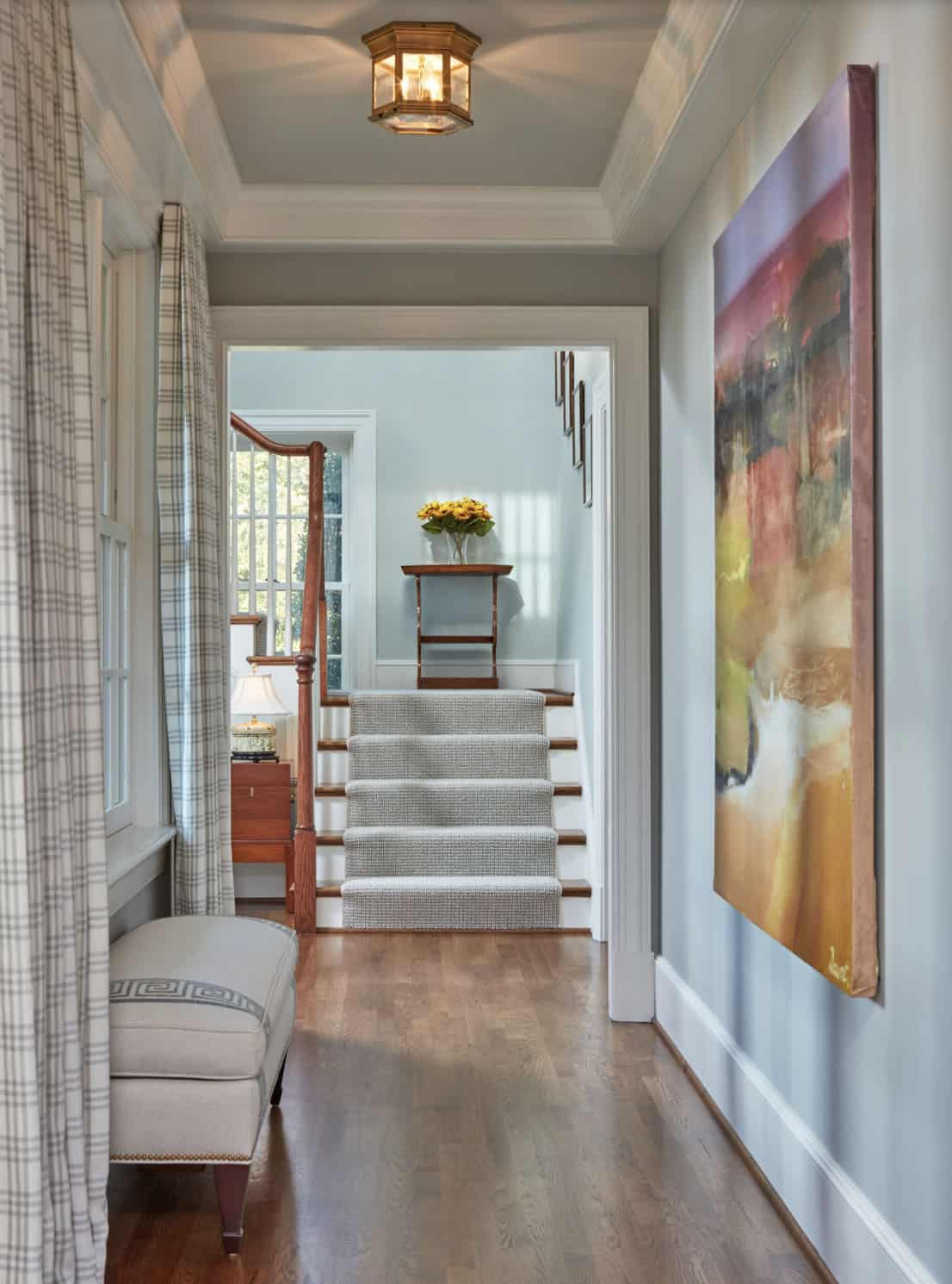 Historic waterfront house interior hallway with coffered ceiling, staircase with carpet runner, abstract artwork and hardwood floors in Maryland