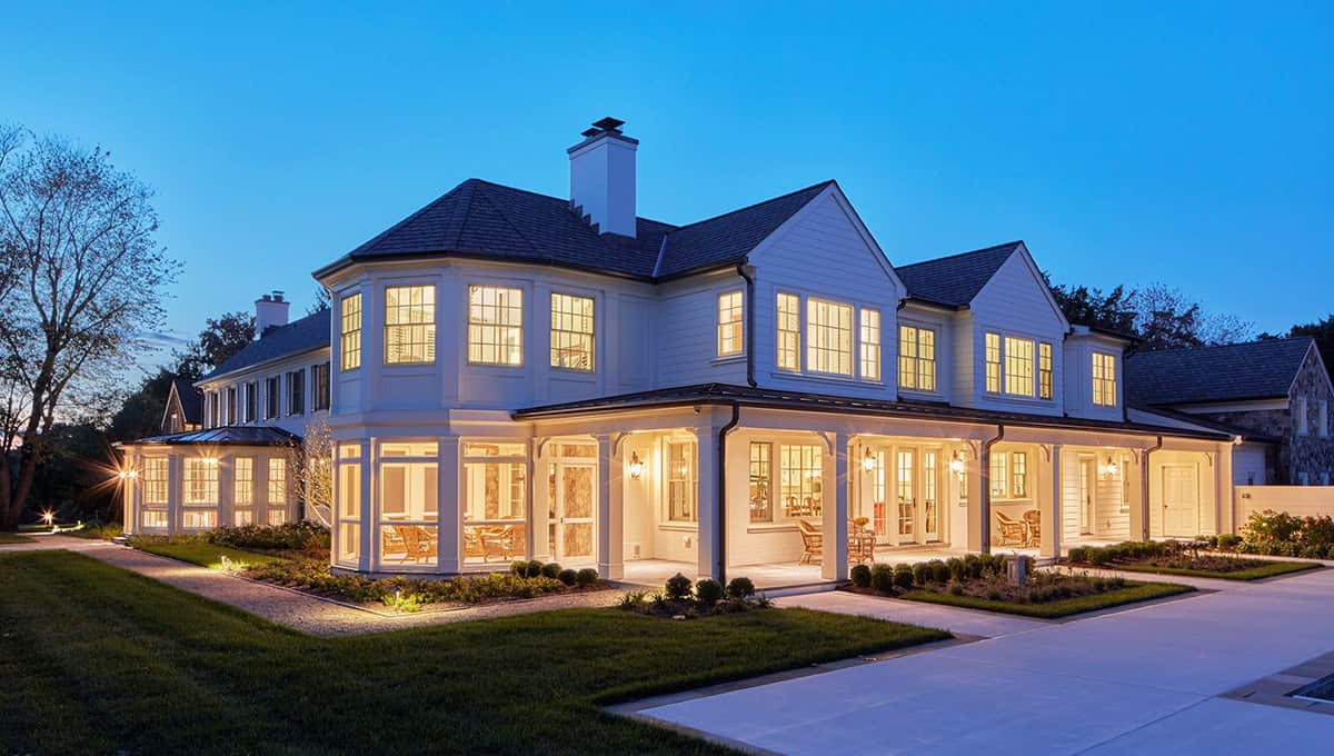 Historic waterfront house side exterior with faceted bay window, wraparound screened porch and landscape lighting at dusk in Maryland
