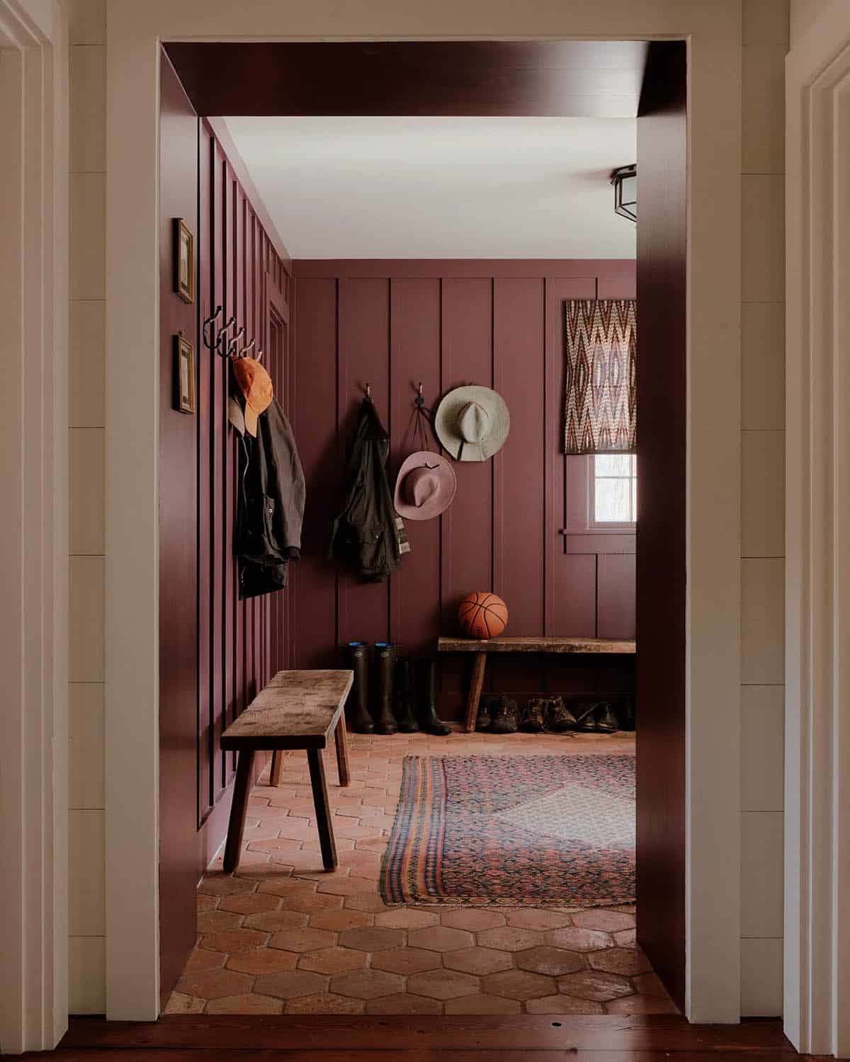 Mudroom with deep burgundy vertical shiplap walls, terracotta hex tile floor, wooden benches, and coat hooks
